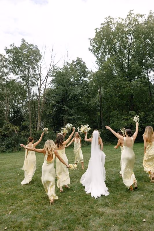 Bride and bridesmaids running across a green lawn