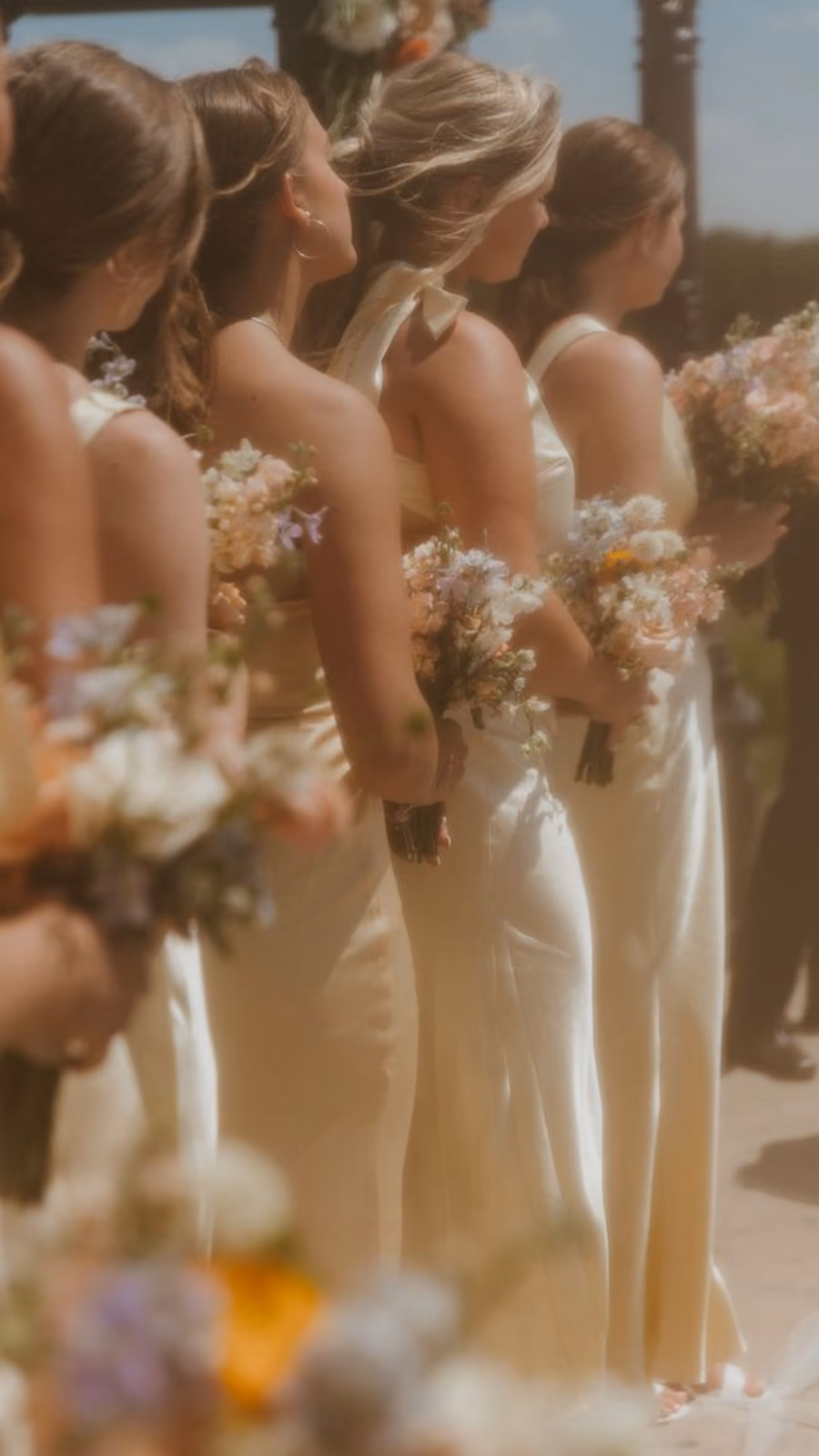 Bridesmaids in pale yellow dresses holding bouquets