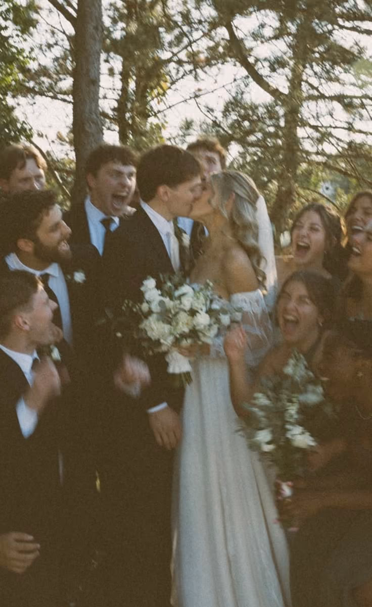 Bride and groom kissing while friends cheer outdoors